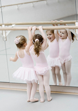 Kleinkind im rosa Tütü vor dem Spiegel an der Ballettstange